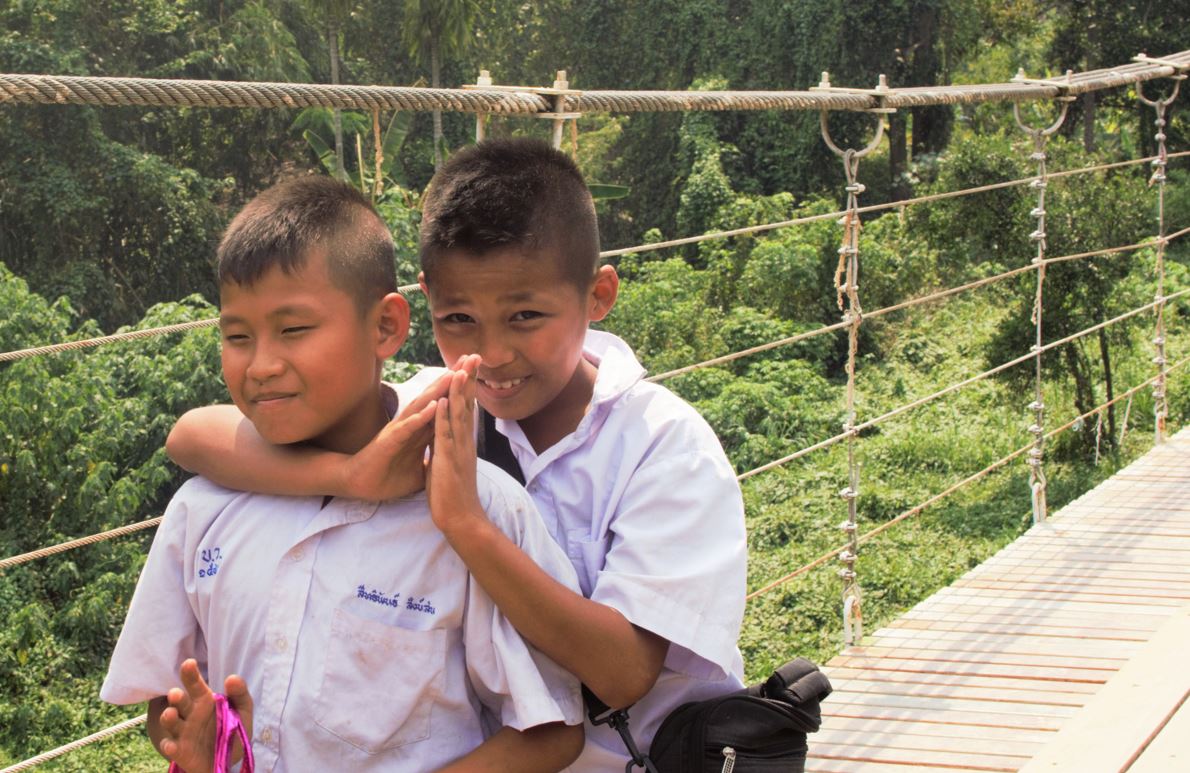 Снимка: Константина Славейкова, деца се връщат от училище по въжен мост в джунглата. Жестът отправен от момчето вдясно е будистки поздрав.